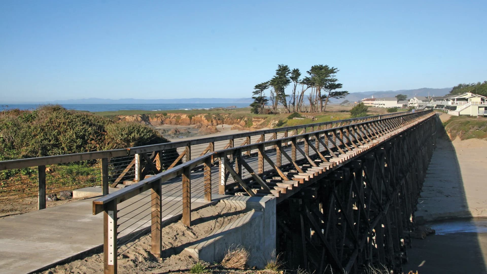 A wooden bridge extends over a coastal area, with ocean and cliffs in the background.