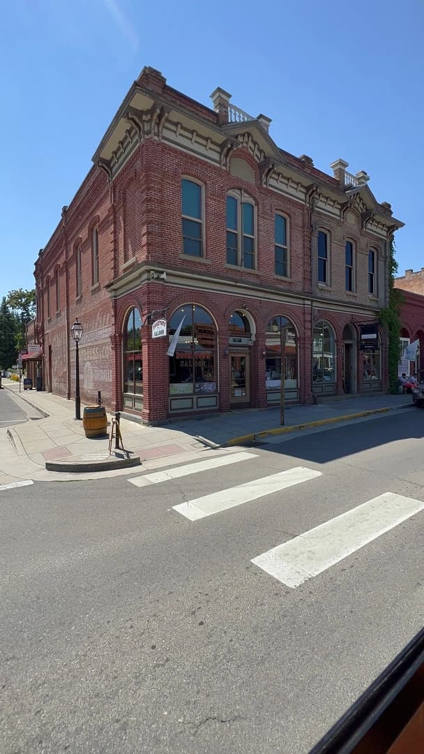 Historic brick building on a corner, featuring arched windows and a saloon sign, against a clear blue sky.