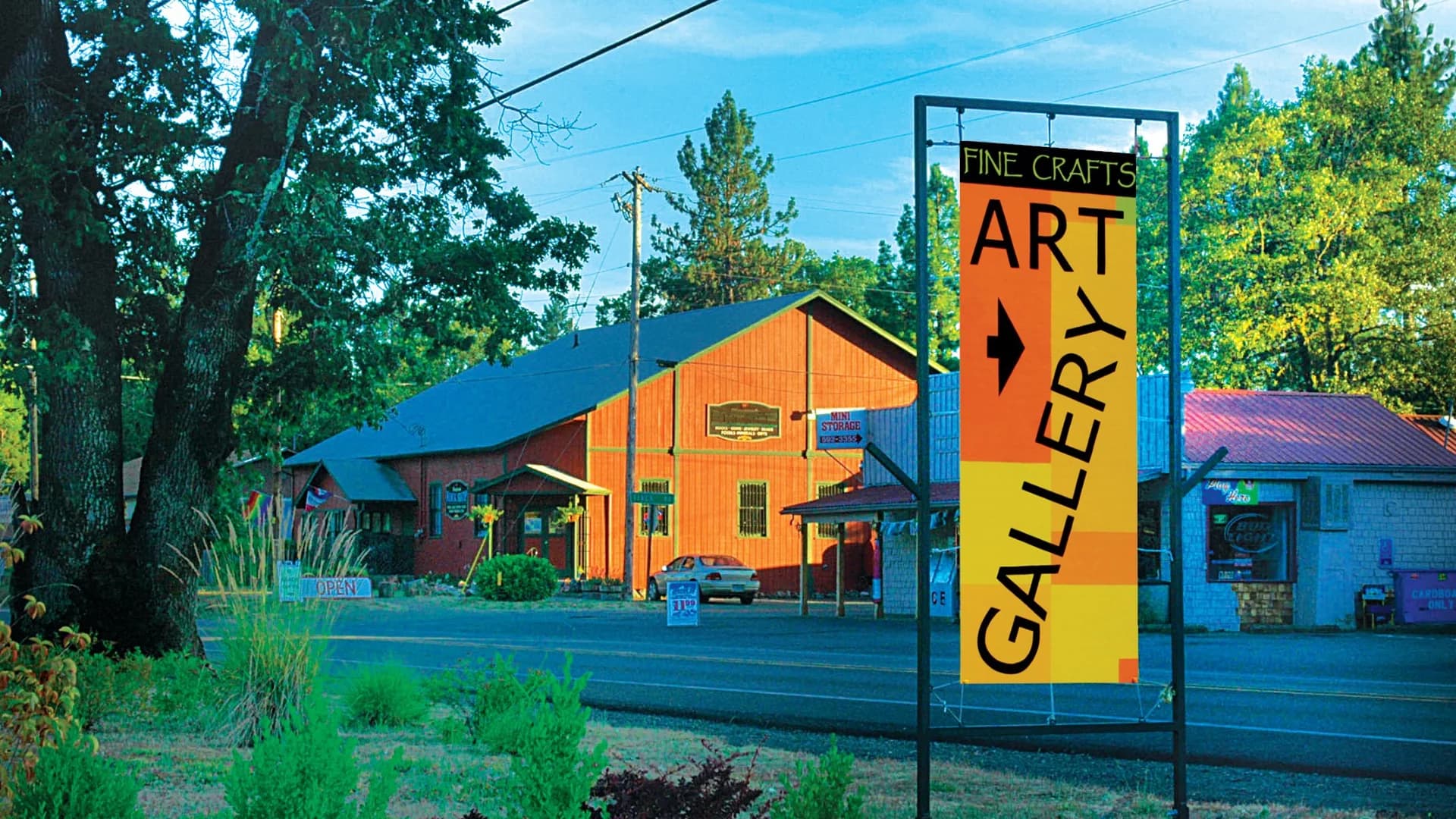Sign for an art gallery and fine crafts, with a red building and trees in the background.