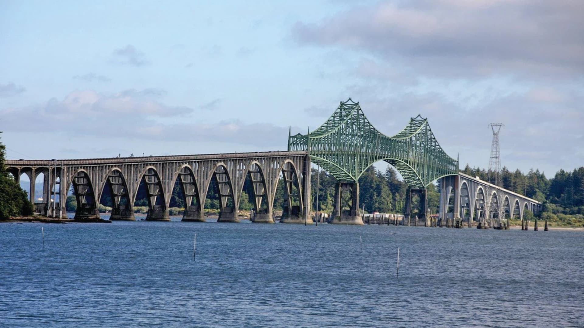 A large, green-and-gray arch bridge spans a river, featuring multiple arches and a scenic forest backdrop.