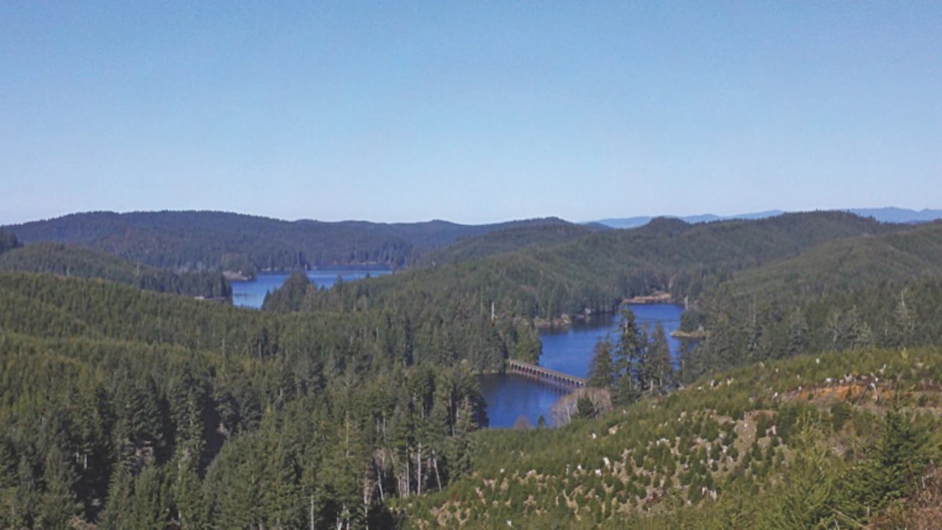 A scenic view of lush green hills and a tranquil lake under a clear blue sky.