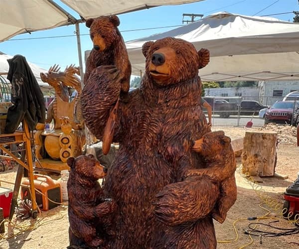 Two large carved wooden bears standing on display under a tent at an outdoor market.